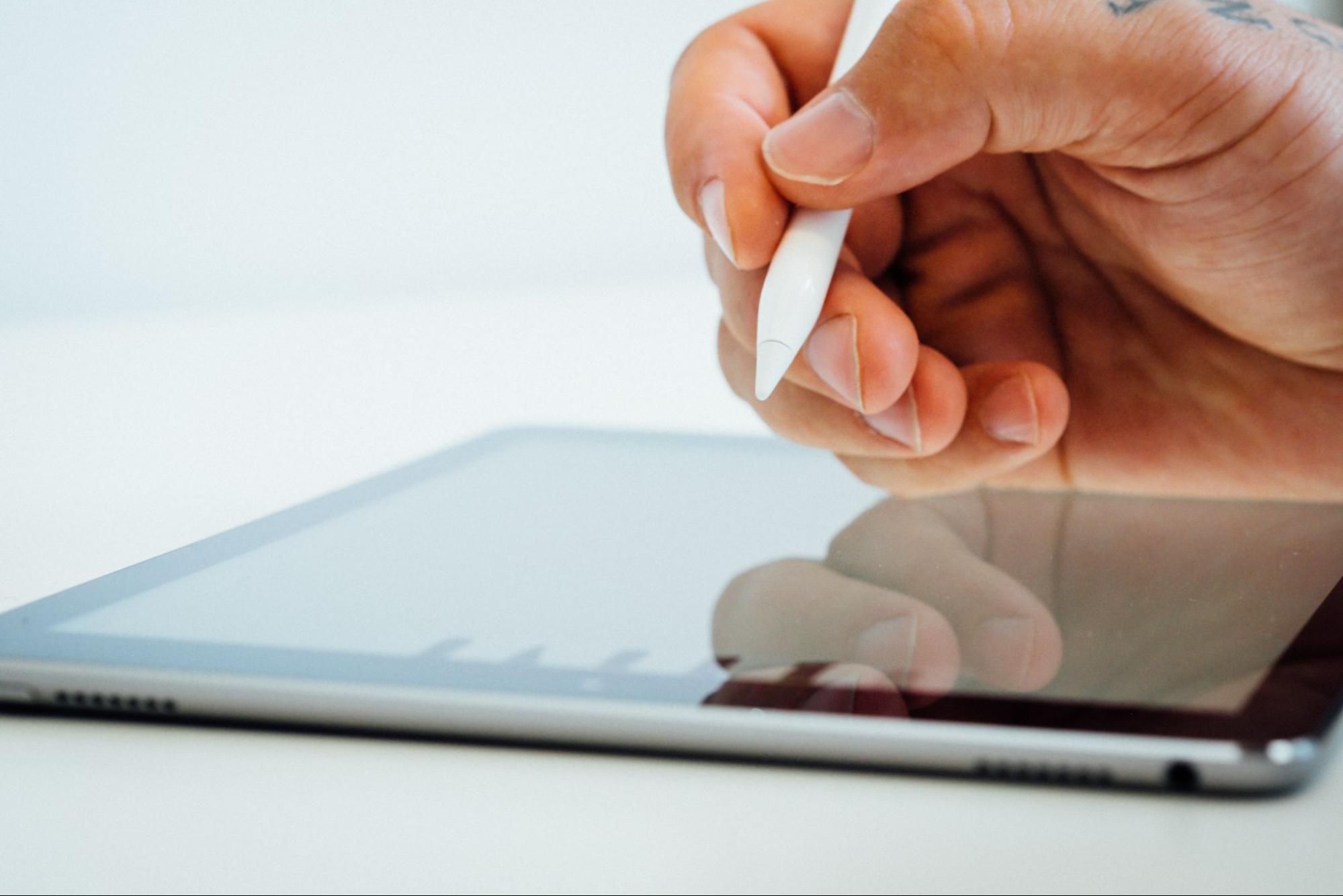 A hand holding a stylus pen over an iPad.