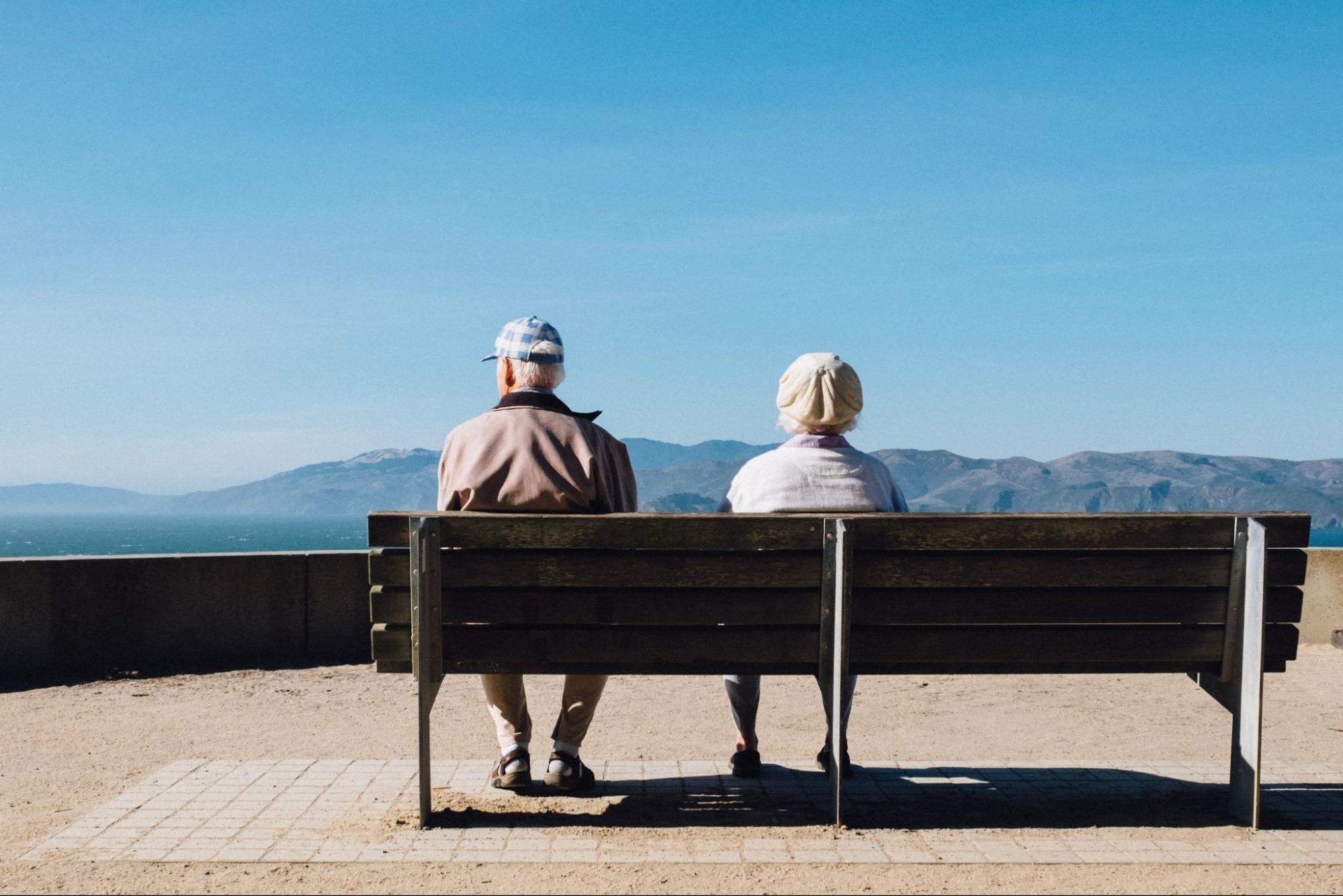 An older couple sitting on a bench with a view of the mountains.