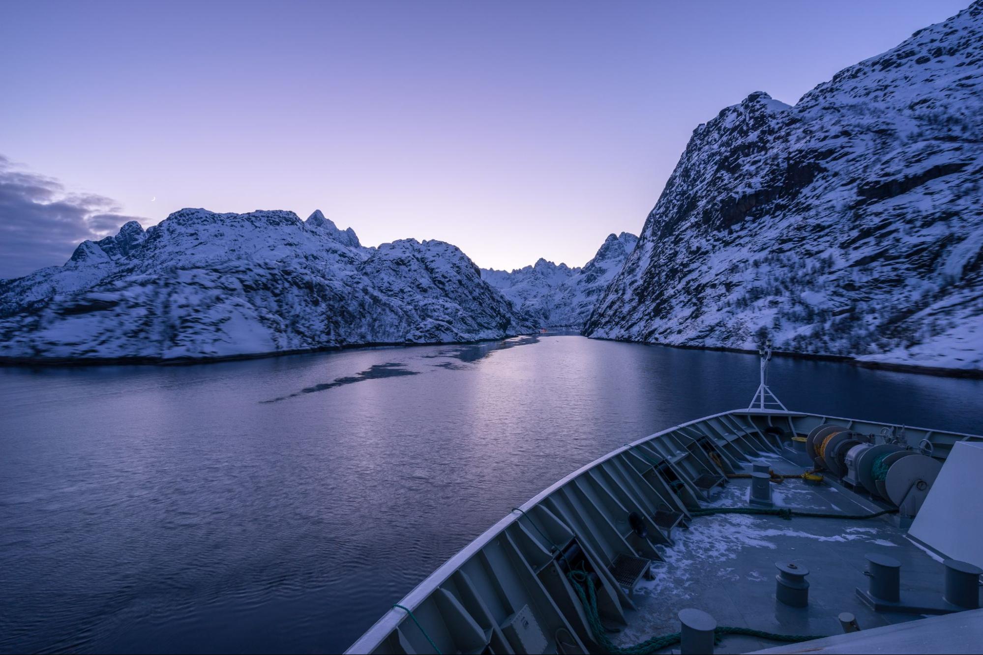 A boat on a body of water with snow covered mountains.