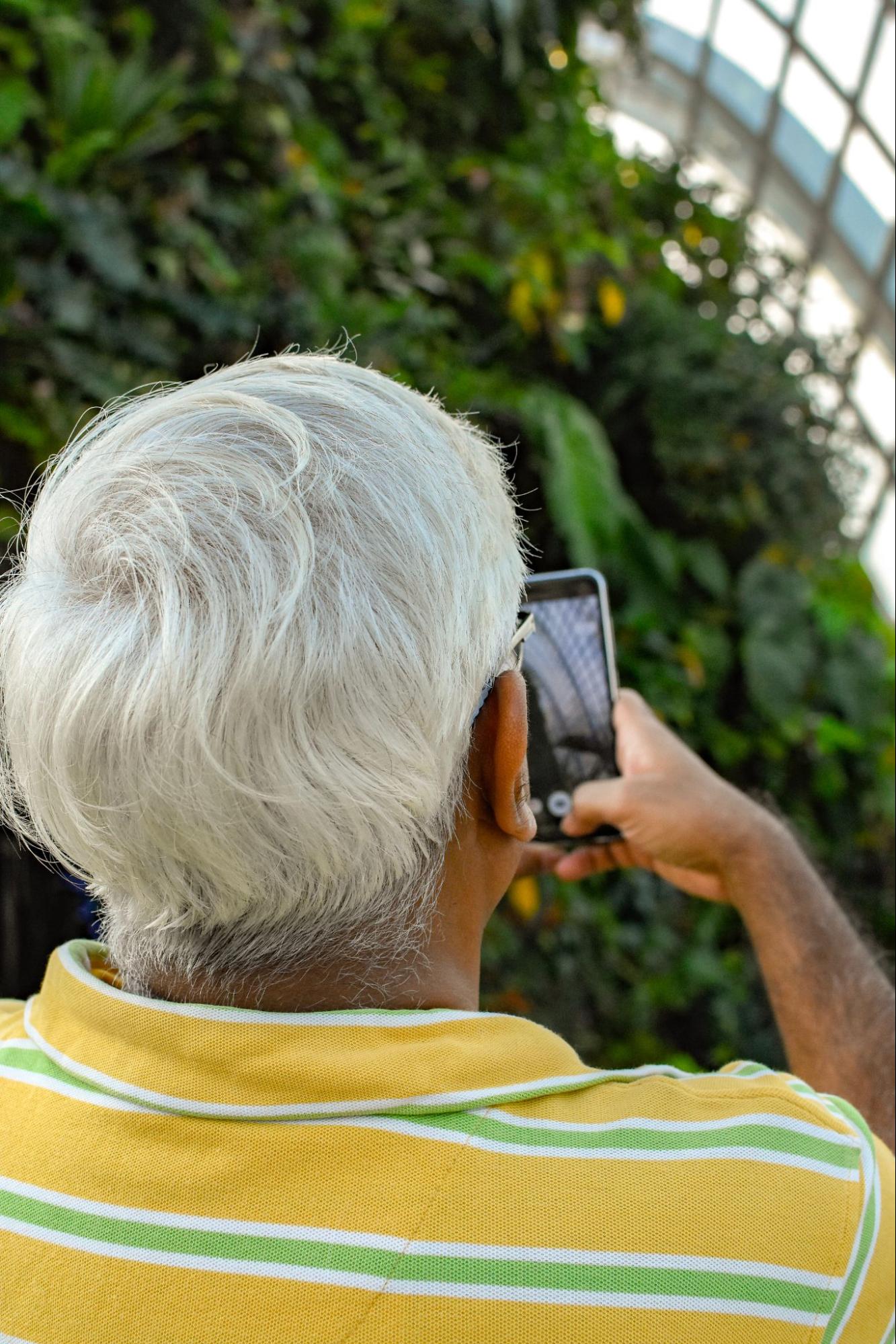 An older man taking a photo of nature with a phone.