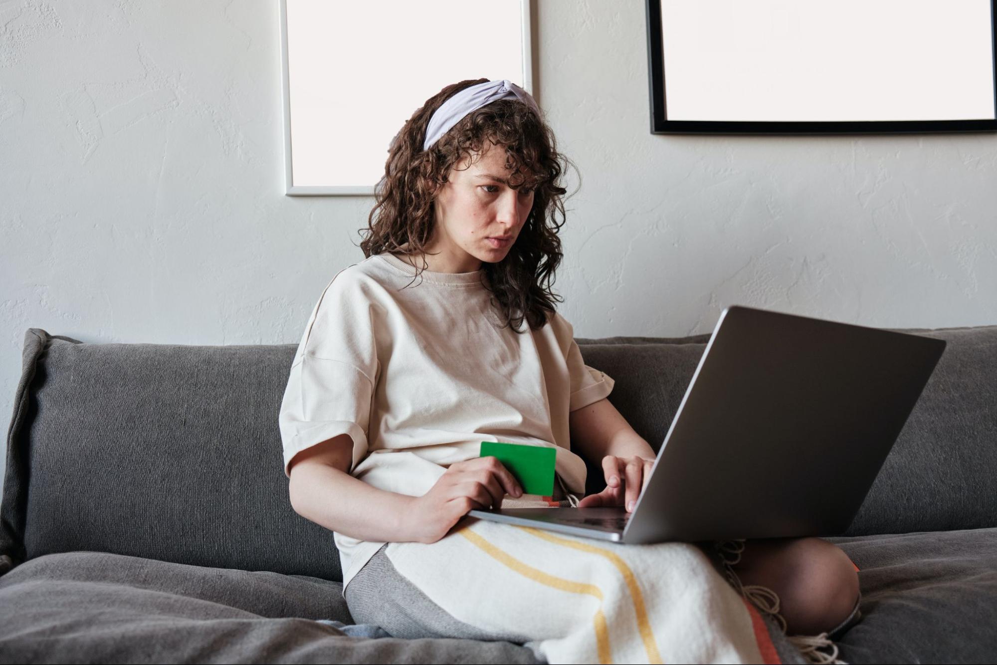 A person sitting on a couch with a laptop and bank card.