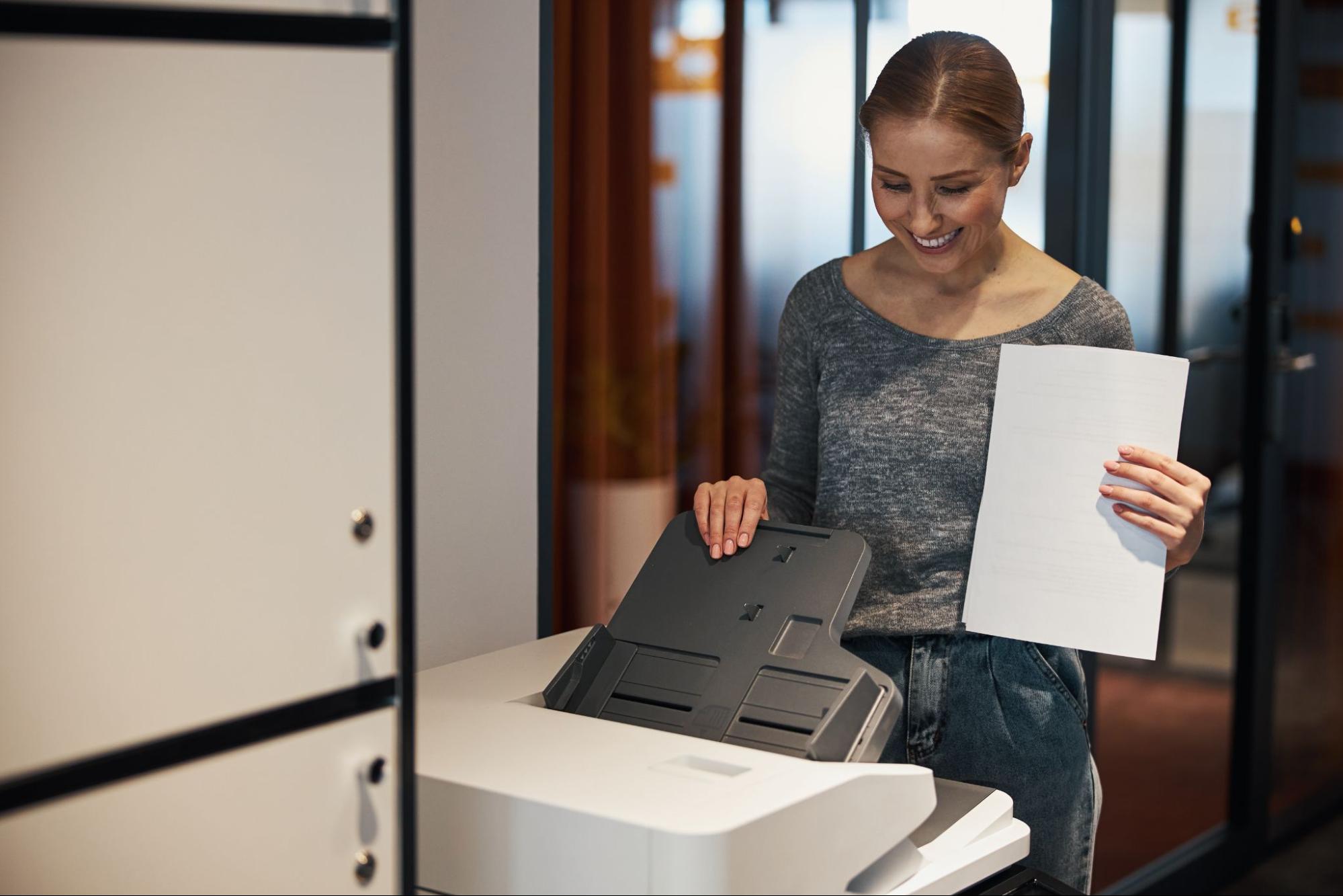 A woman standing in front of a printer with paper sheets.