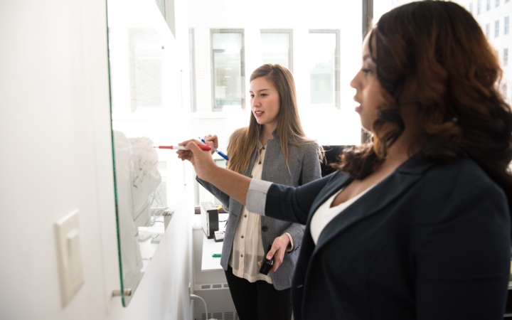 Two women looking at a whiteboard.