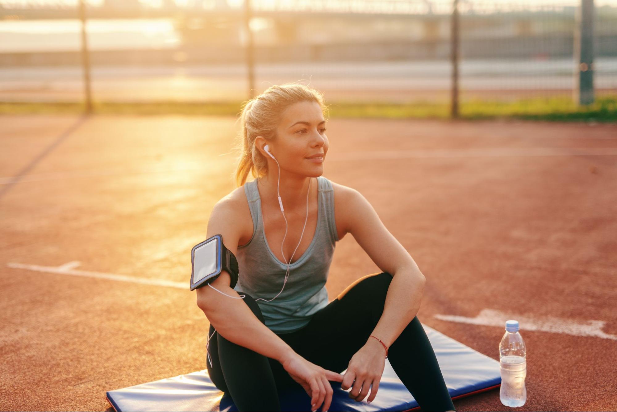 A person sitting on a mat with earphones and a bottle of water.